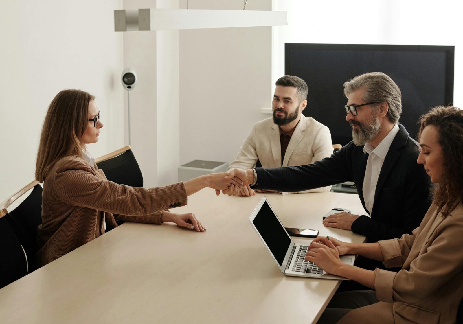 Business professionals engaging in a handshake across a conference table, signifying successful collaboration.